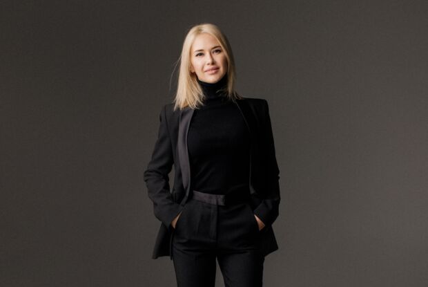 A lady wearing a black suit with a casual look, her hands in her pockets.
